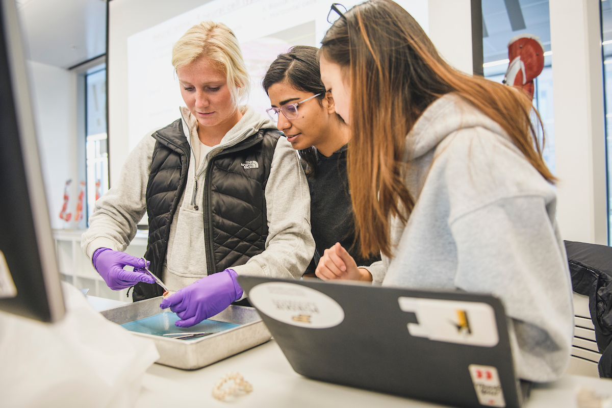 Pictured: students and faculty standing around a science lab tabel